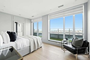 A modern hotel room with a large bed, a sofa, a small table, and a view of the city through large windows. - 2BR Entertainment District Hub | Balcony & Parking | Parking Available (Toronto)