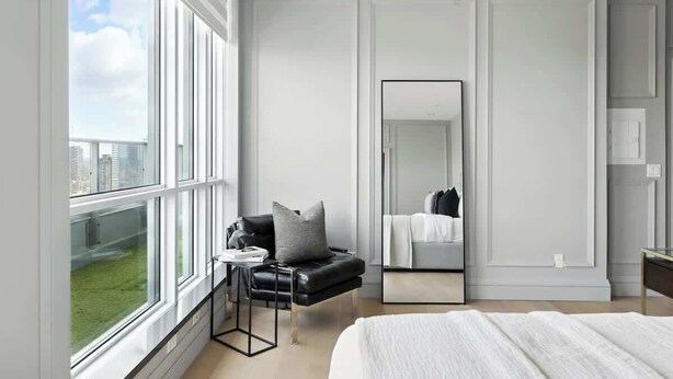 Quarto moderno com uma janela grande, uma cama, área de estar com uma poltrona e um espelho.
