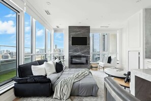 A modern living room with a large window, a fireplace, a sofa, and a television. - 2BR Entertainment District Hub | Balcony & Parking | Parking Available (Toronto)