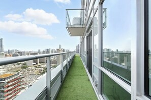 A narrow balcony with a green artificial grass floor, large windows, and a cityscape view. - 2BR Entertainment District Hub | Balcony & Parking | Parking Available (Toronto)