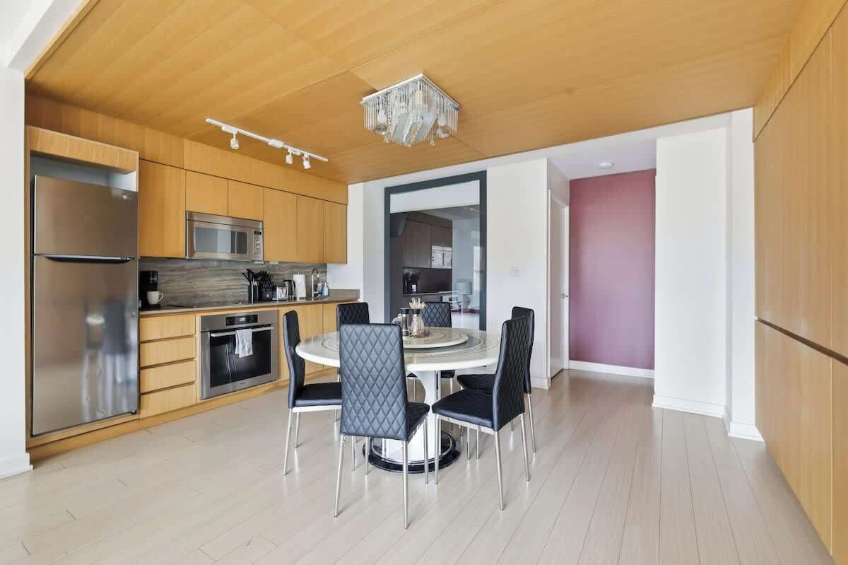 A modern kitchen with a dining area, wooden cabinets, stainless steel appliances, and a chandelier.