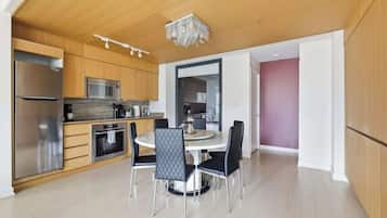 A modern kitchen with a dining area, wooden cabinets, stainless steel appliances, and a chandelier.