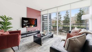 Una sala de estar moderna con un televisor de pantalla plana, un sofá rojo, un sofá negro y una mesa de centro de vidrio.