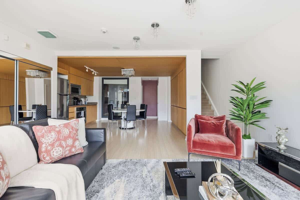 A modern living room with a sofa, a red chair, a coffee table, and a dining area in the background.