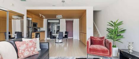 Una sala de estar moderna con un sofá, una silla roja, una mesita de centro y un comedor al fondo.