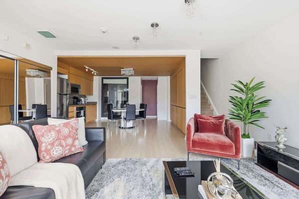 A modern living room with a sofa, a red chair, a coffee table, and a dining area in the background.