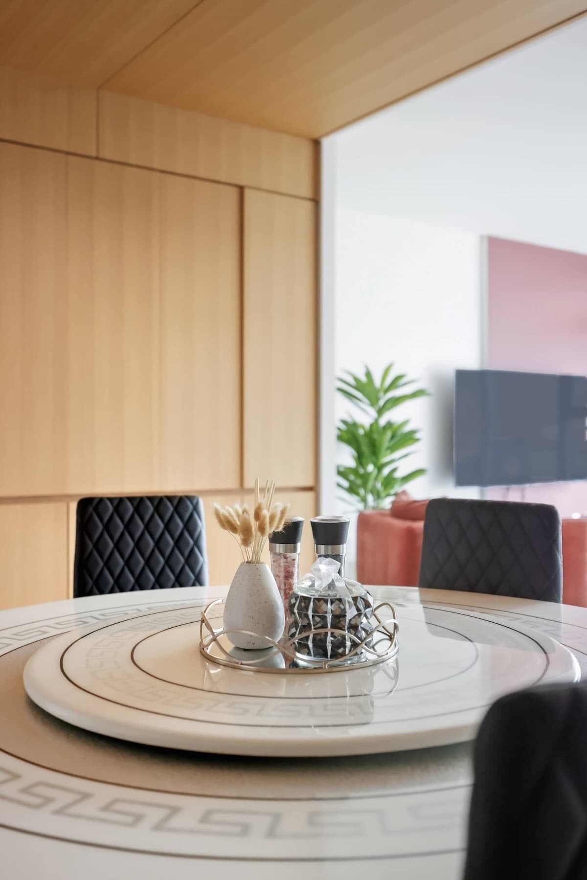 Une table ronde avec un plateau en marbre blanc, un vase blanc contenant des fleurs séchées et deux salières et poivrières noires.