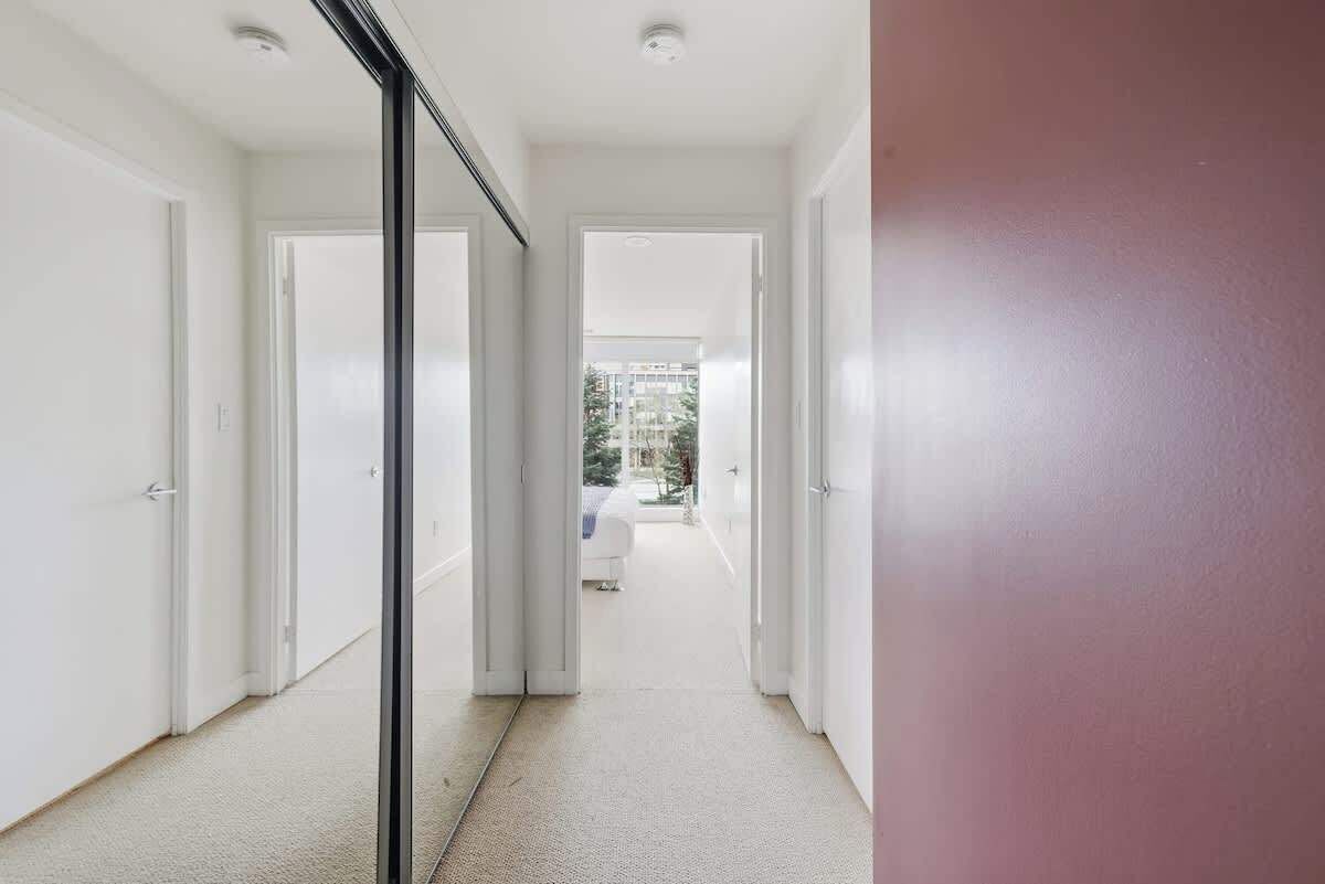 A corridor with white doors leading to a balcony with a view of greenery.
