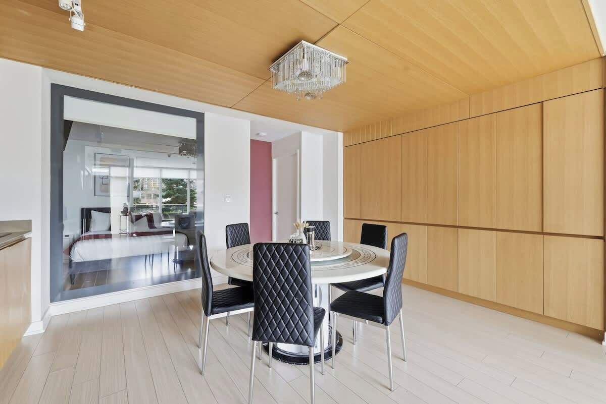 A modern dining area with a round table, black cushioned chairs, and a chandelier.