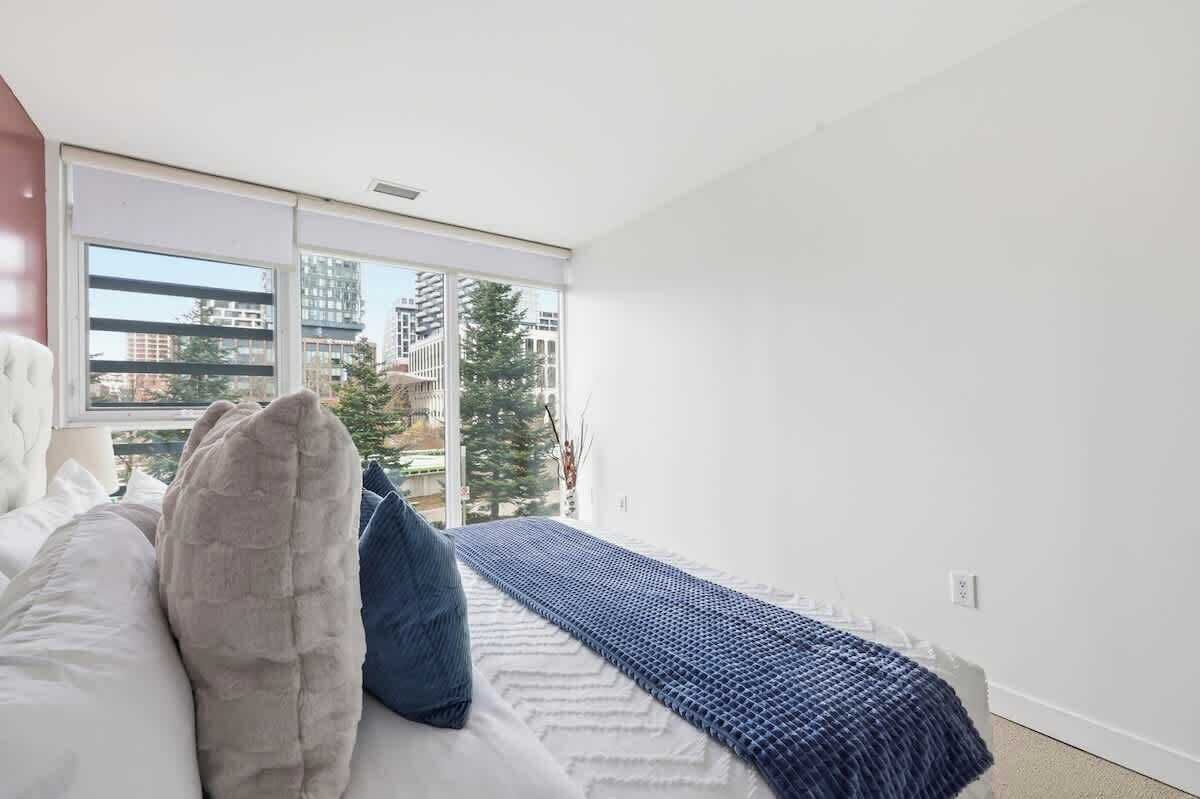 A bedroom with a bed, a window, and a view of buildings.