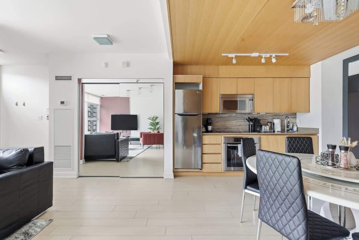 A modern kitchen with stainless steel appliances, a dining area with a round table and chairs, and a living area with a sofa and TV.
