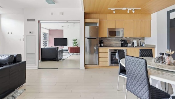 Una cocina moderna con electrodomésticos de acero inoxidable, un comedor con una mesa redonda y sillas, y una sala de estar con sofá y televisor.