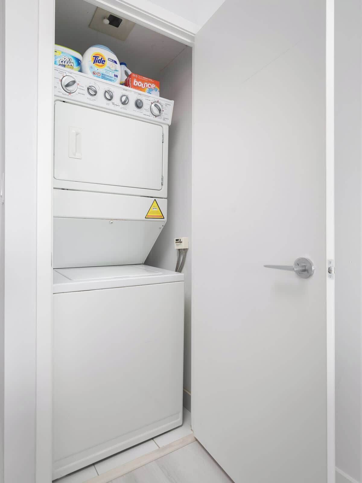 Une petite buanderie blanche, équipée d’un lave-linge et d’un sèche-linge superposés.