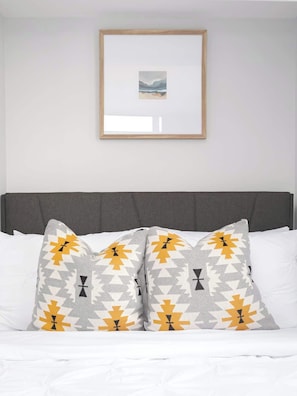 A bed with a grey headboard, white bedding, and patterned pillows.
