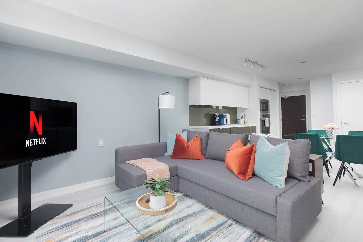Una sala de estar moderna con un televisor de pantalla plana, sofá gris y una mesa de centro con una planta.