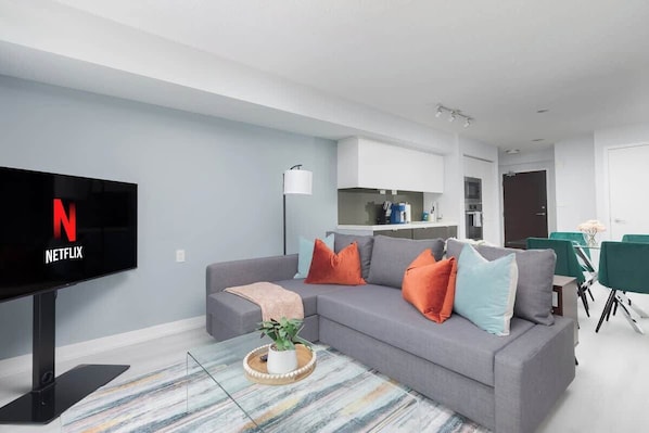 A modern living room with a flat-screen TV, grey sofa, and a coffee table with a plant.