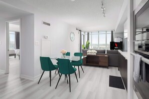 A modern apartment with a dining area, kitchenette, and a living space with a large window.