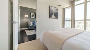 A bedroom with a large bed, a city view, a gray sofa, and a painting on the wall. - Modern City Escape 1-BR Retreat Downtown Toronto (Toronto)