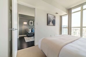 A bedroom with a large bed, a city view, a gray sofa, and a painting on the wall. - Modern City Escape 1-BR Retreat Downtown Toronto (Toronto)