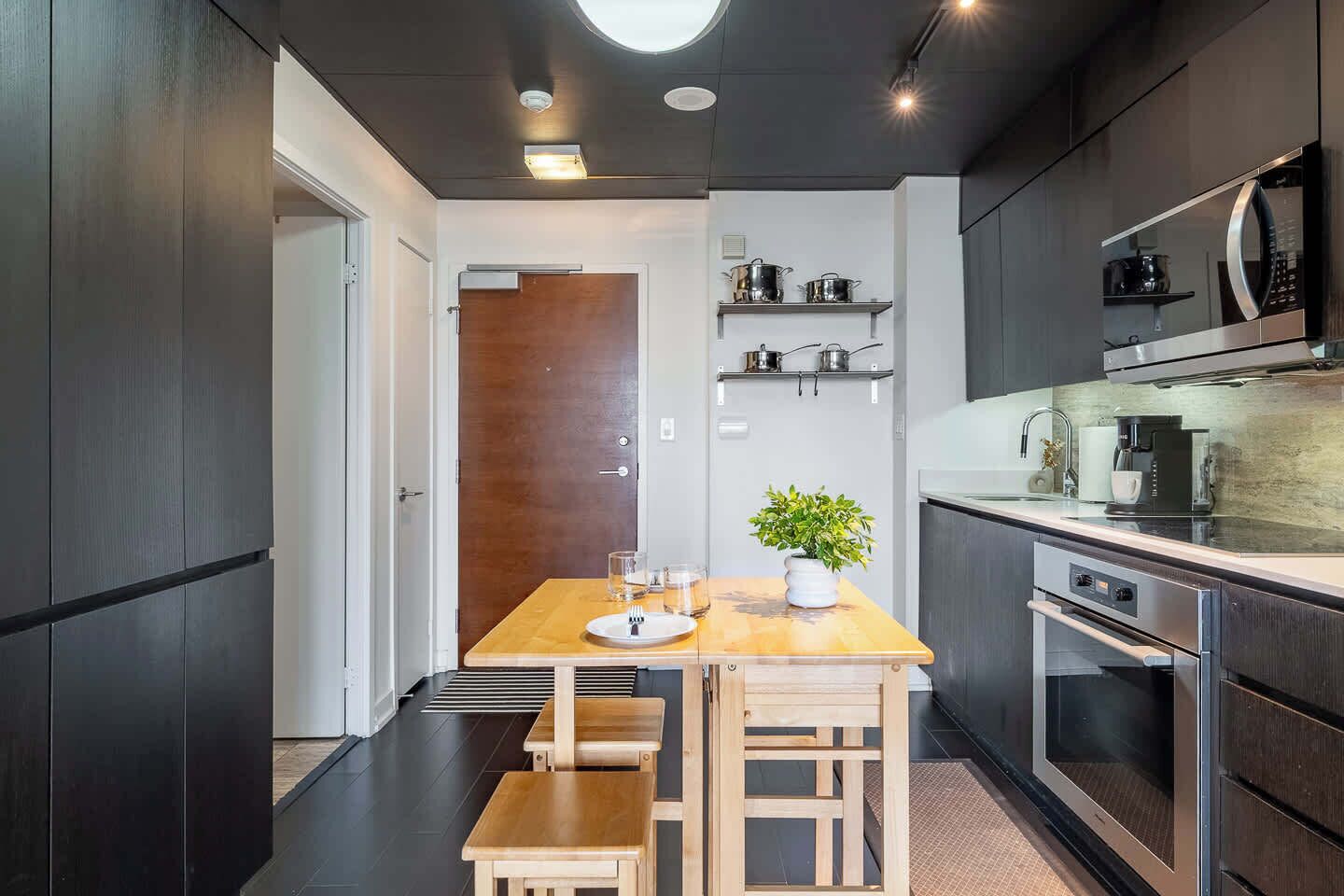 A compact kitchen with a wooden table, a bench, a potted plant, and modern appliances.