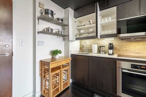A modern kitchen with dark cabinetry, stainless steel appliances, and open shelving for dishes and cookware. - Modern City Escape 1-BR Retreat Downtown Toronto (Toronto)