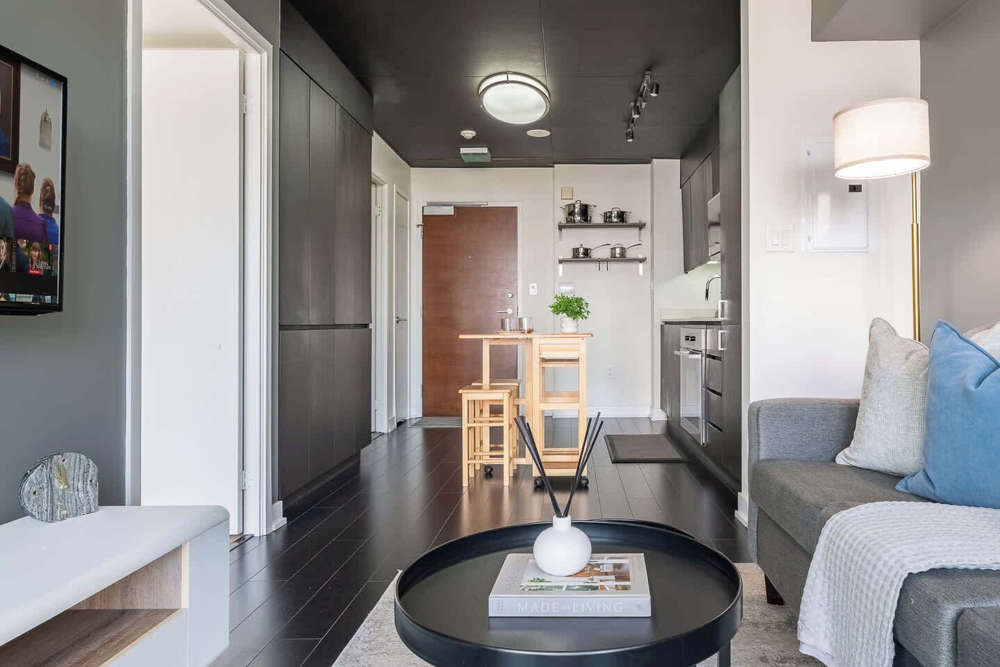 Un salon moderne avec un canapé, une table basse sur laquelle repose un livre, et une cuisine en arrière-plan.