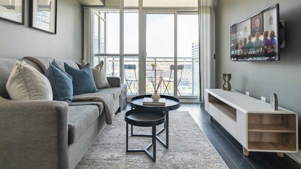 A modern living room with a sofa, a coffee table, and a TV mounted on the wall. - Modern City Escape 1-BR Retreat Downtown Toronto (Toronto)