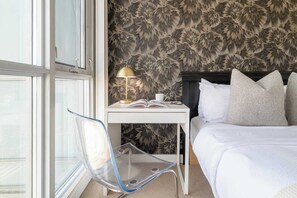 Ein Hotelzimmer mit Bett, Nachttisch mit Lampe, Stuhl und Fenster.