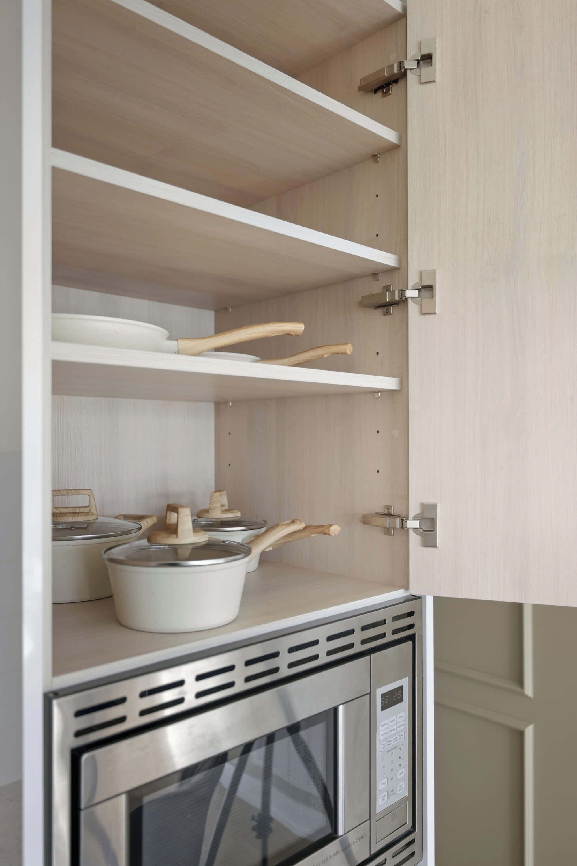Una cocina con horno microondas integrado, utensilios de madera y una olla sobre la encimera.