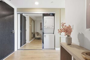 A hallway with a modern, minimalist design, leading to a room with a washing machine and a vase of flowers on a wooden table.