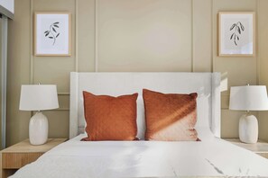 Ein Hotelzimmer mit einem großen Bett, zwei Kissen, zwei Nachttischlampen und zwei gerahmten Kunstwerken an der Wand.