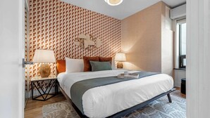 Habitación de hotel moderna con una cama grande, dos mesitas de noche, un papel tapiz decorativo y una ventana.