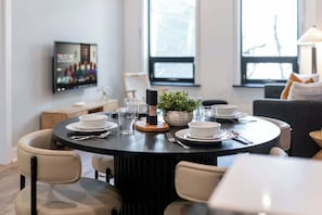 A dining area with a round table set for four, chairs, a television on the wall, and a window with a view. - Downtown 1BR near Elm Street | King Bed | Parking Available (Toronto)