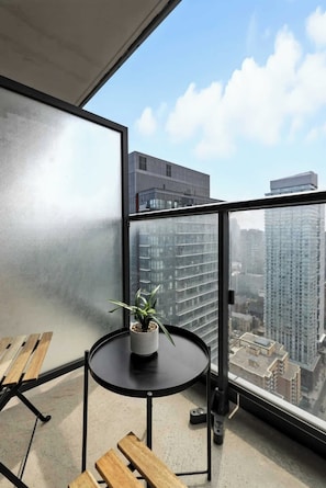Ein Balkon mit Blick auf hohe Gebäude, ein runder Tisch mit einem Blumentopf und Holzmöbel.