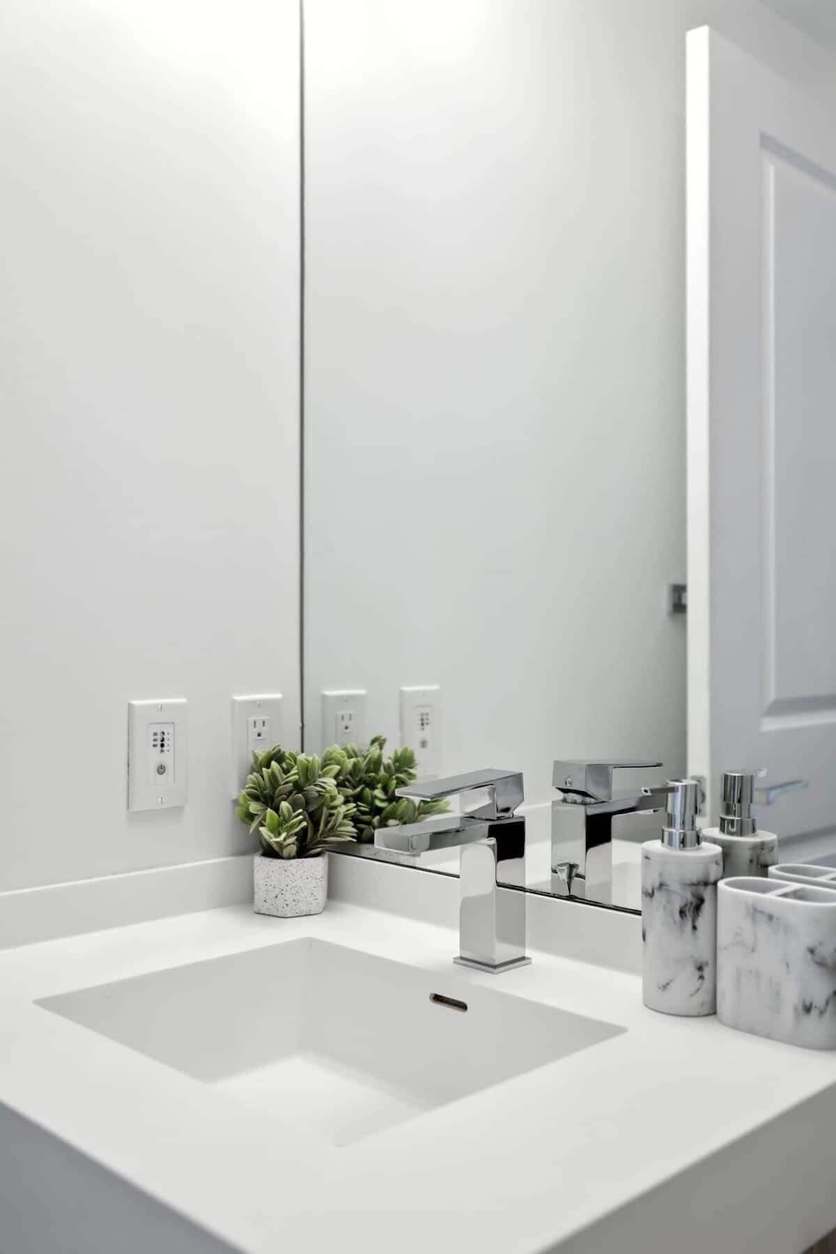 Un baño moderno con un espejo grande, un lavamanos blanco y una planta en maceta.