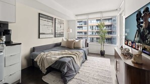 A modern bedroom with a bed, a television, a window with a view of a building, and a potted plant. - Stylish 1BR Lakeside Oasis Patio & Prime Location (Toronto)
