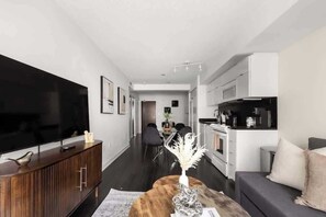 Un salon moderne avec un téléviseur à écran plat, des meubles en bois foncé et un coin repas à l’arrière-plan.