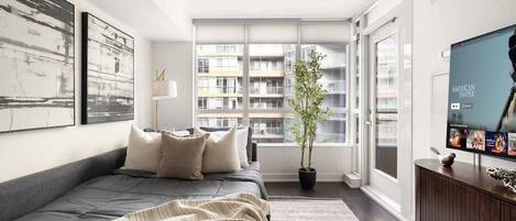 Un dormitorio moderno con una cama grande, una planta en maceta, un televisor y vistas de un edificio alto.