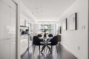 A modern kitchen with a dining area, featuring a glass partition, dark flooring, and contemporary furniture. - Stylish 1BR Lakeside Oasis Patio & Prime Location | Parking Available (Toronto)