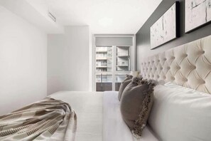 Une chambre à coucher avec un grand lit, une fenêtre donnant sur des immeubles et un mur orné de tableaux encadrés.