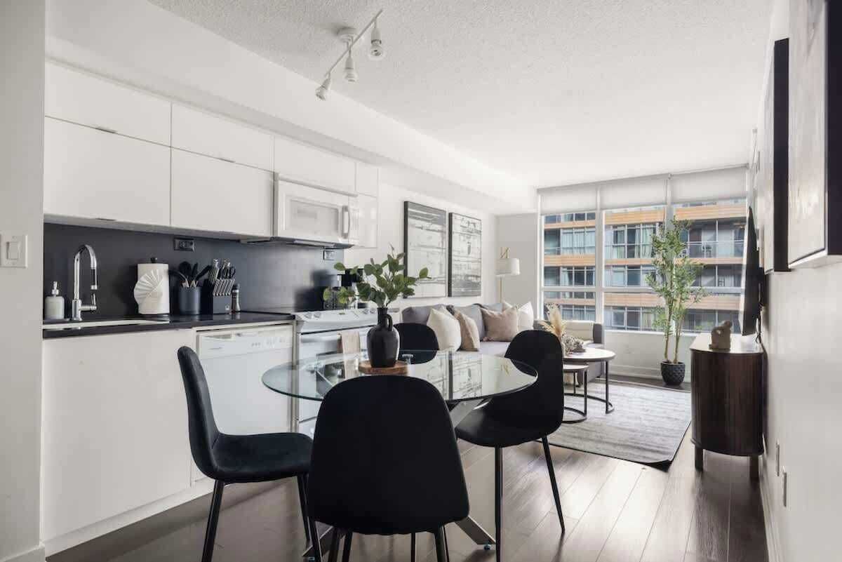 Una cocina moderna con armarios blancos, una mesa de comedor de vidrio y sillas negras.