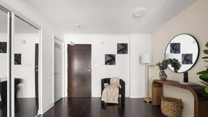 A modern interior with a dark wood floor, a black chair, a mirror, and a console table with a vase. - Stylish 1BR Lakeside Oasis Patio & Prime Location (Toronto)