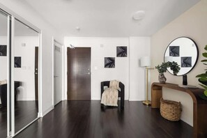 Ein modernes Interieur mit dunklem Holzboden, einem schwarzen Sessel, einem Spiegel und einem Konsolentisch mit einer Vase.