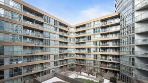 A multi-story residential building with a central courtyard, balconies, and a mix of glass and wooden facade elements. - Stylish 1BR Lakeside Oasis Patio & Prime Location (Toronto)