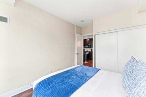 Un dormitorio con cama, un armario blanco y una kitchenette al fondo.