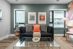 A modern living room with a dark grey sofa, a glass coffee table, and two framed pictures on the wall. - Serene Downtown Stay, steps to Mount Sinai | Parking Available (Toronto)