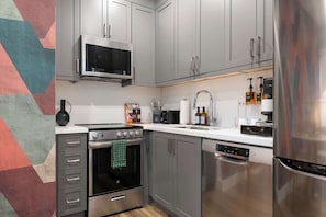 A modern kitchen with stainless steel appliances, grey cabinetry, and a microwave above the stove. - Serene Downtown Stay, steps to Mount Sinai | Parking Available (Toronto)