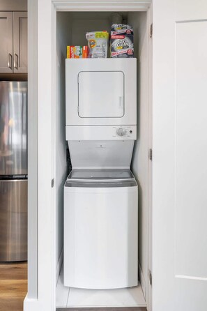 Eine kompakte, weiße Waschmaschine mit Bedienfeld und einer transparenten Tür, eingebaut in einen schmalen Schrank mit Stauraum darüber.