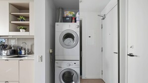 Uma lavanderia compacta com máquinas de lavar empilhadas, uma pequena cozinha com uma torradeira e uma porta que dá para outro quarto.