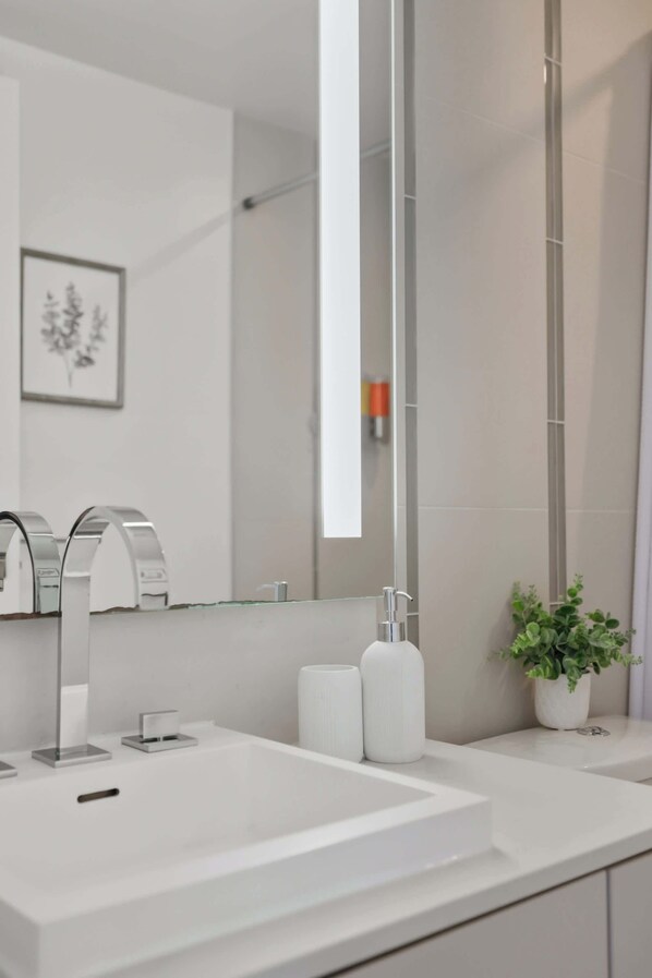 A modern bathroom with a large mirror, a white sink, and a potted plant.